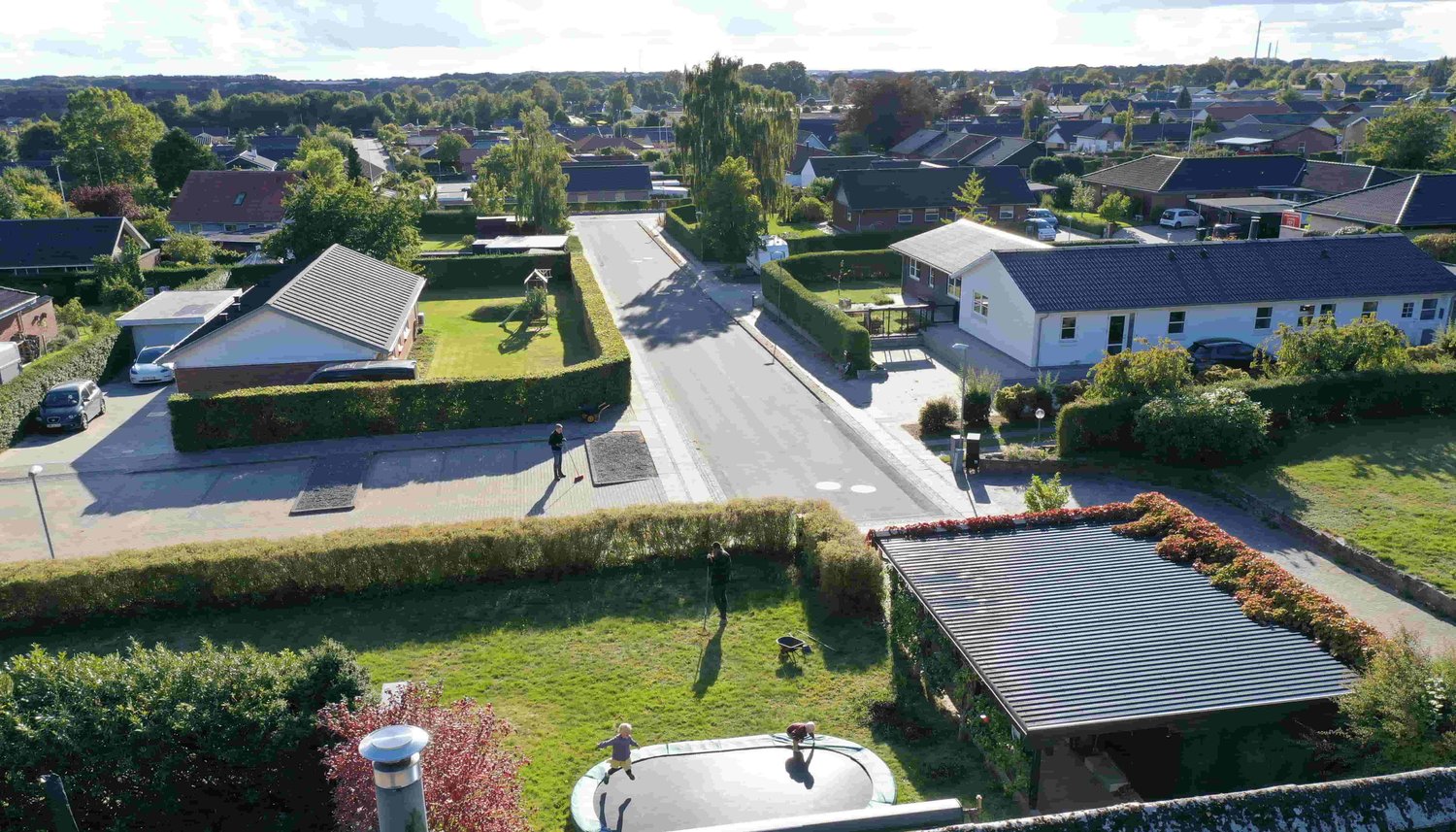 Dronefoto af naboer der taler sammen mens børn hopper i trampolin