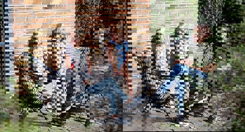 Familie sidder på lille terrasse ved bolig og nyder solen